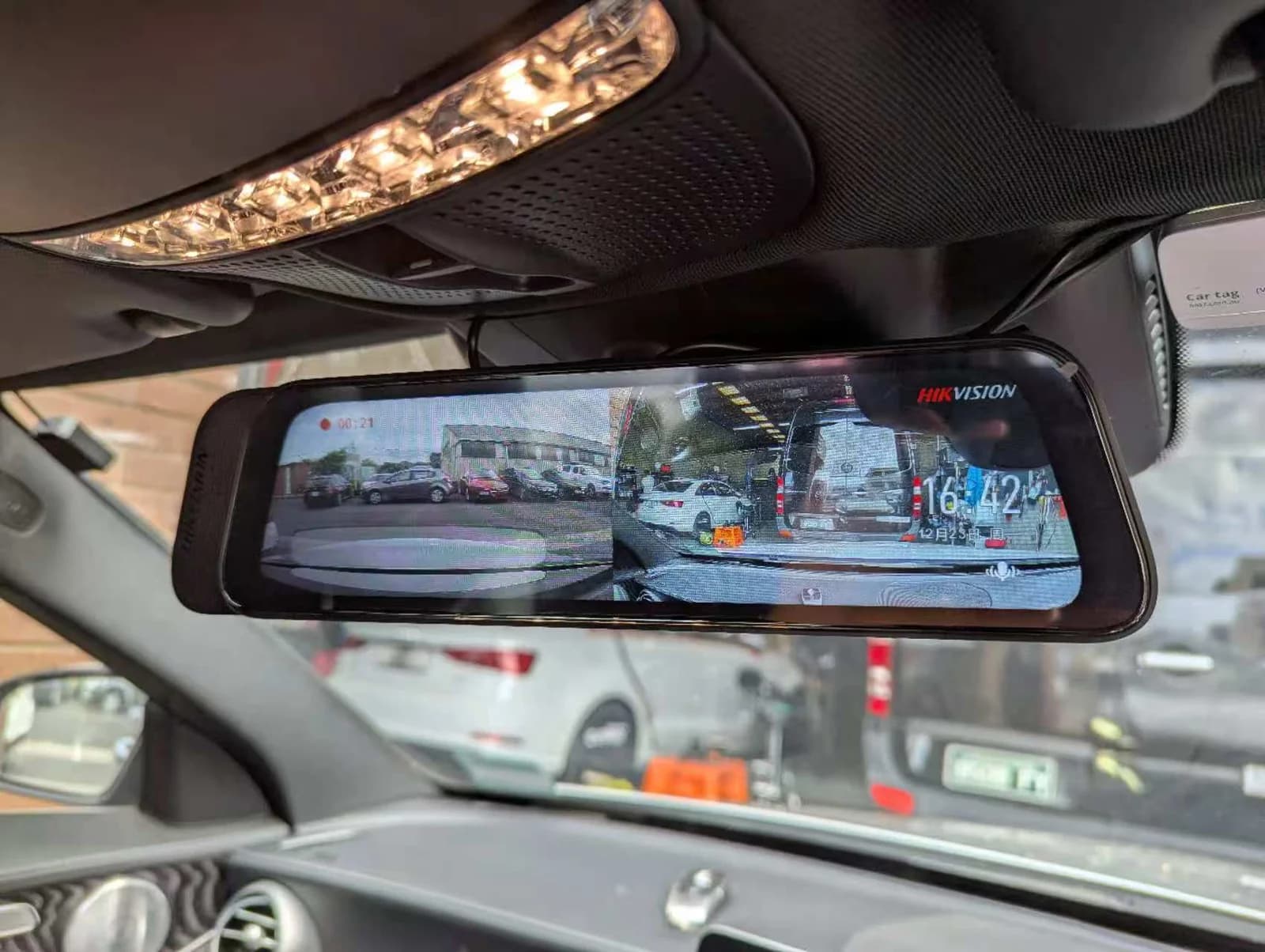 Mirror-style dual-view dash cam unit installed in a Mercedes-Benz C-Class showing front and rear feeds on screen