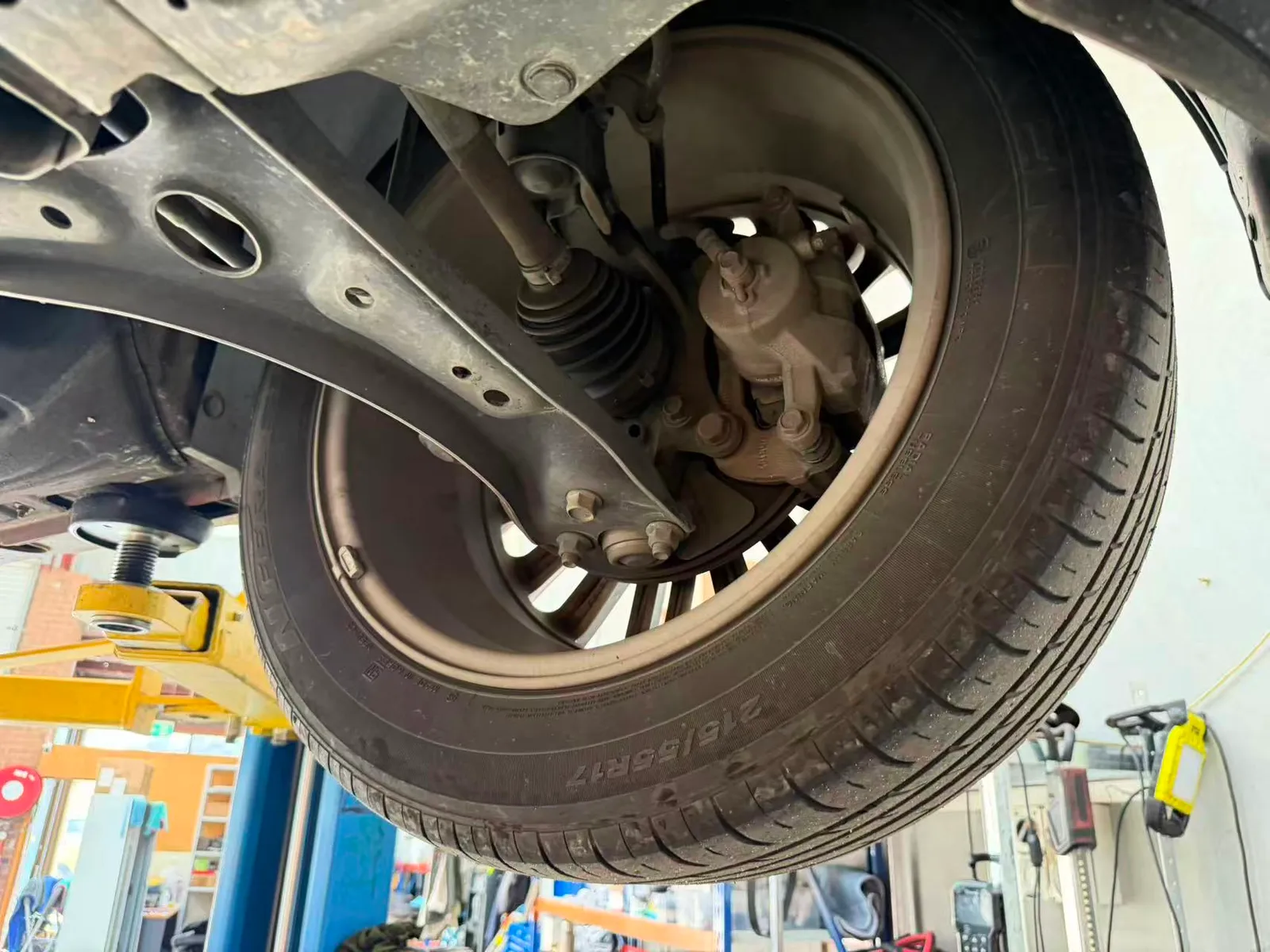 Front corner of a Hyundai Kona on the hoist showing the tyre, brake caliper, driveshaft boot and lower control arm during inspection