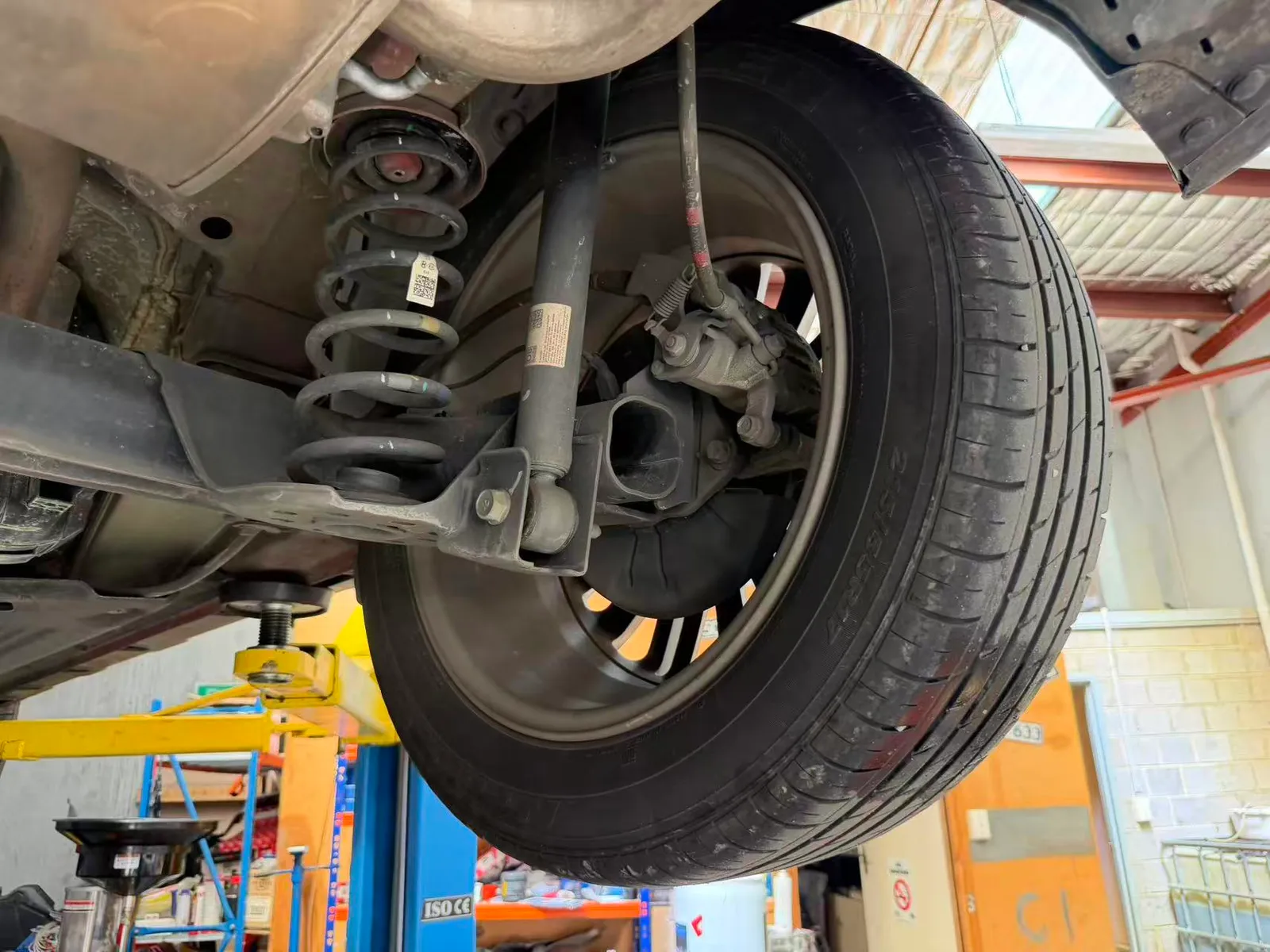 Rear corner of a Hyundai Kona on the hoist showing the coil spring, shock absorber, brake caliper and tyre being inspected