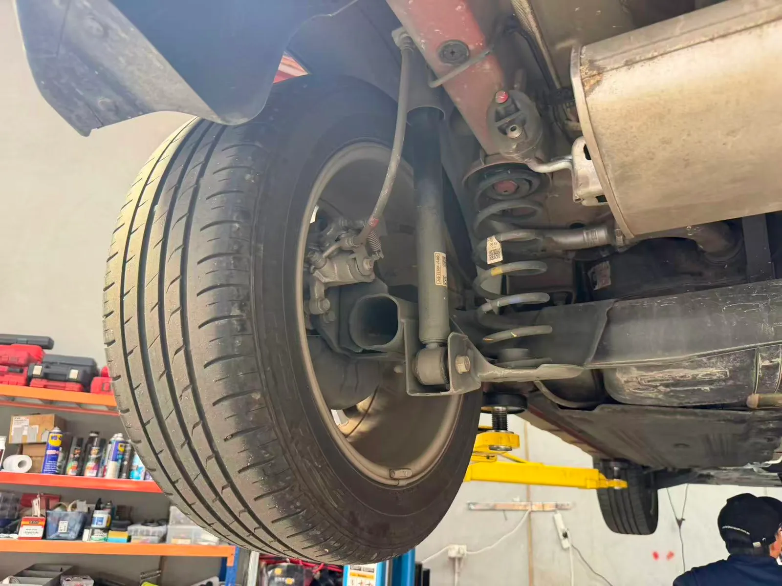 Opposite rear corner of the Hyundai Kona with its spring, shock absorber and brake caliper inspected on the hoist