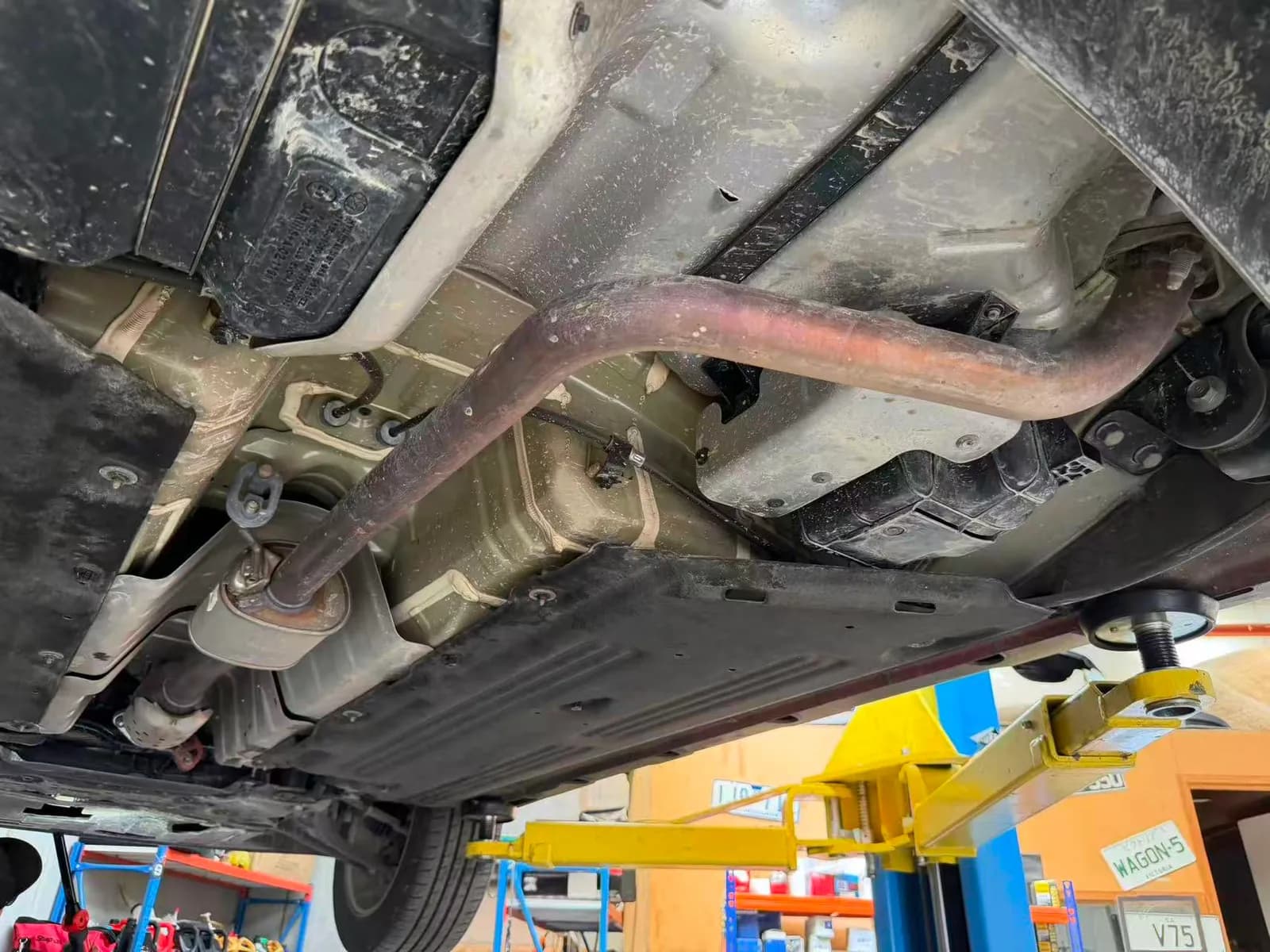 Underside of a Hyundai Kona on the hoist showing the exhaust, muffler, fuel tank and heat shields during inspection