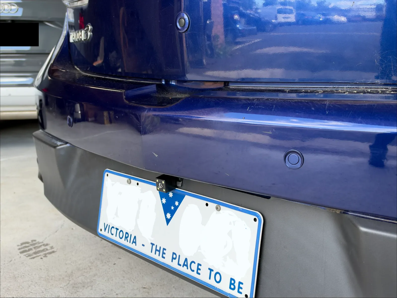 Close view of a painted parking sensor and the reverse camera above the rear number plate of a 2011 Mazda3