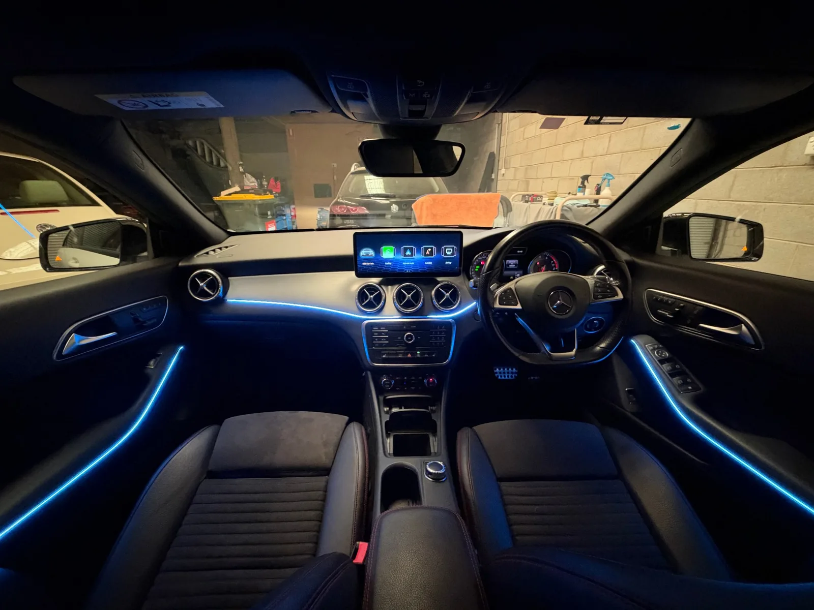 Blue ambient lighting along the dash and both front doors of a 2015 Mercedes-Benz CLA, with a 12.3-inch CarPlay screen on top of the dash