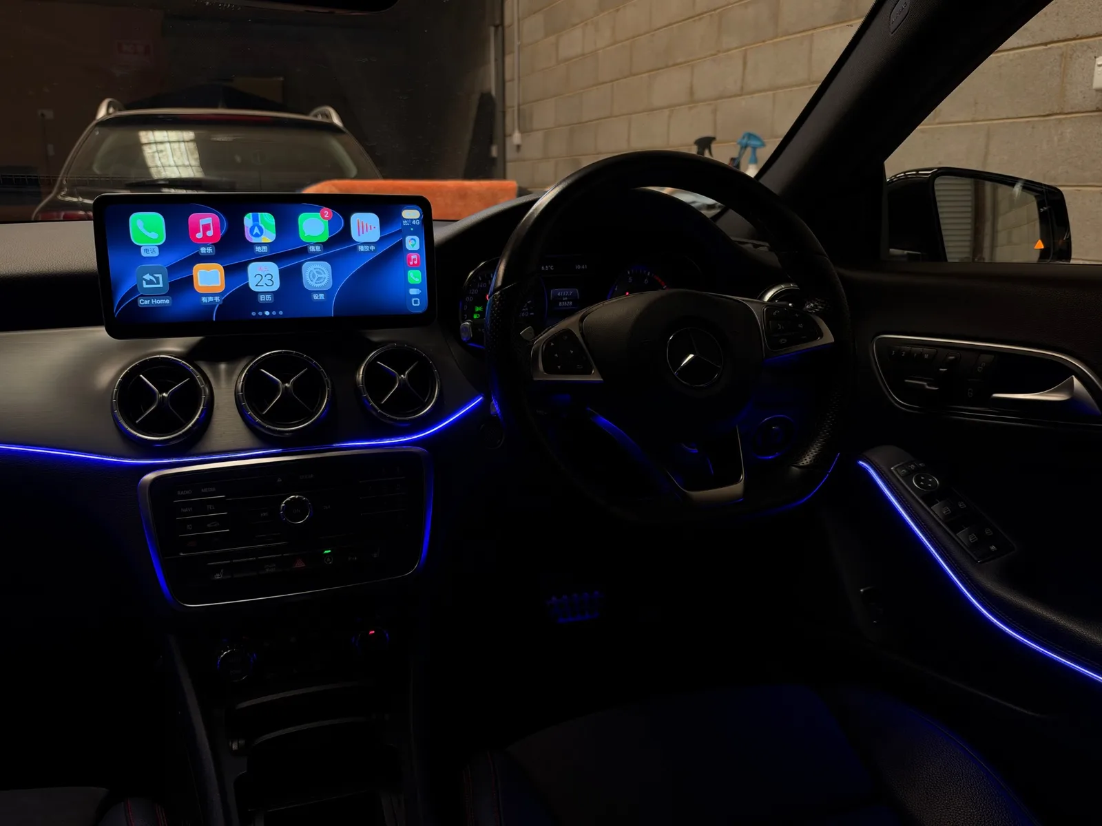Apple CarPlay home screen on the 12.3-inch screen of a 2015 Mercedes-Benz CLA, with blue ambient lighting on the dash and door