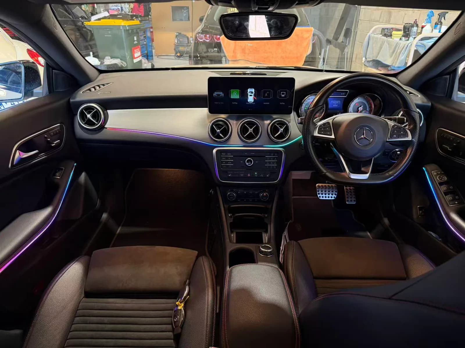 The dash of a 2015 Mercedes-Benz CLA in daylight, with multicolour ambient lighting and the 12.3-inch screen showing CarPlay, Android Auto and AirPlay