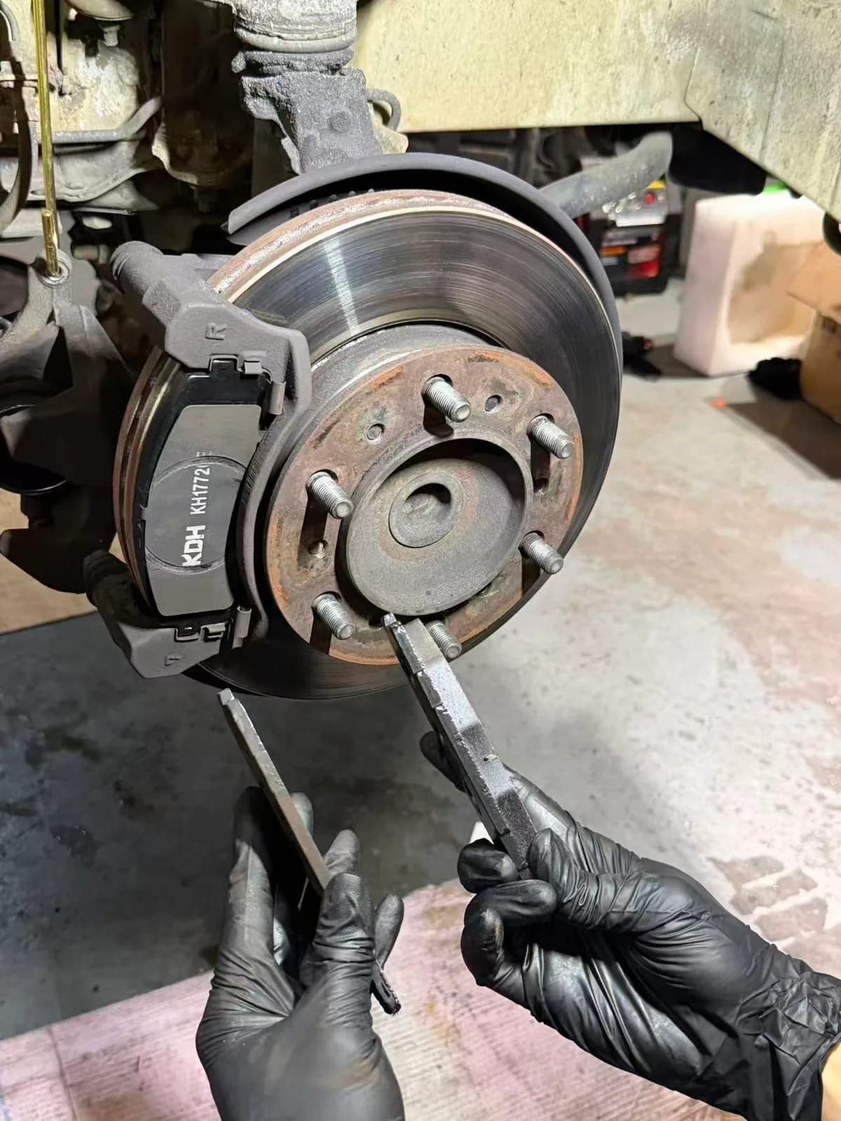 Technician removing worn front brake pads from a Toyota HiAce work van